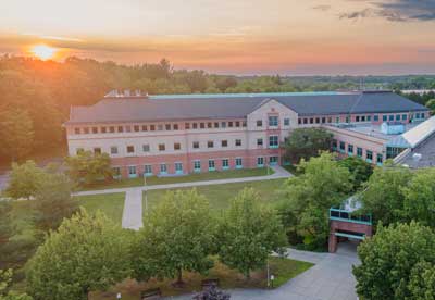 Summer exterior drone shot of the Center for Advanced Materials Processing building with the sun setting in the background over green trees